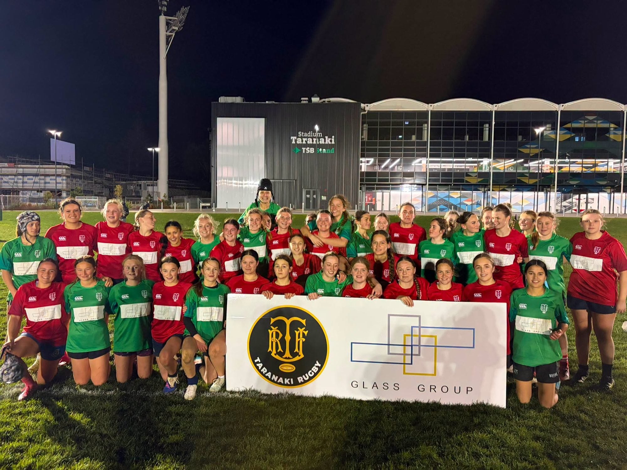 The North and Central squads together behind the Taranaki Rugby and Glass Group banner after game one of the Glass Group Kendra Cocksedge Tournament at Stadium Taranaki.
